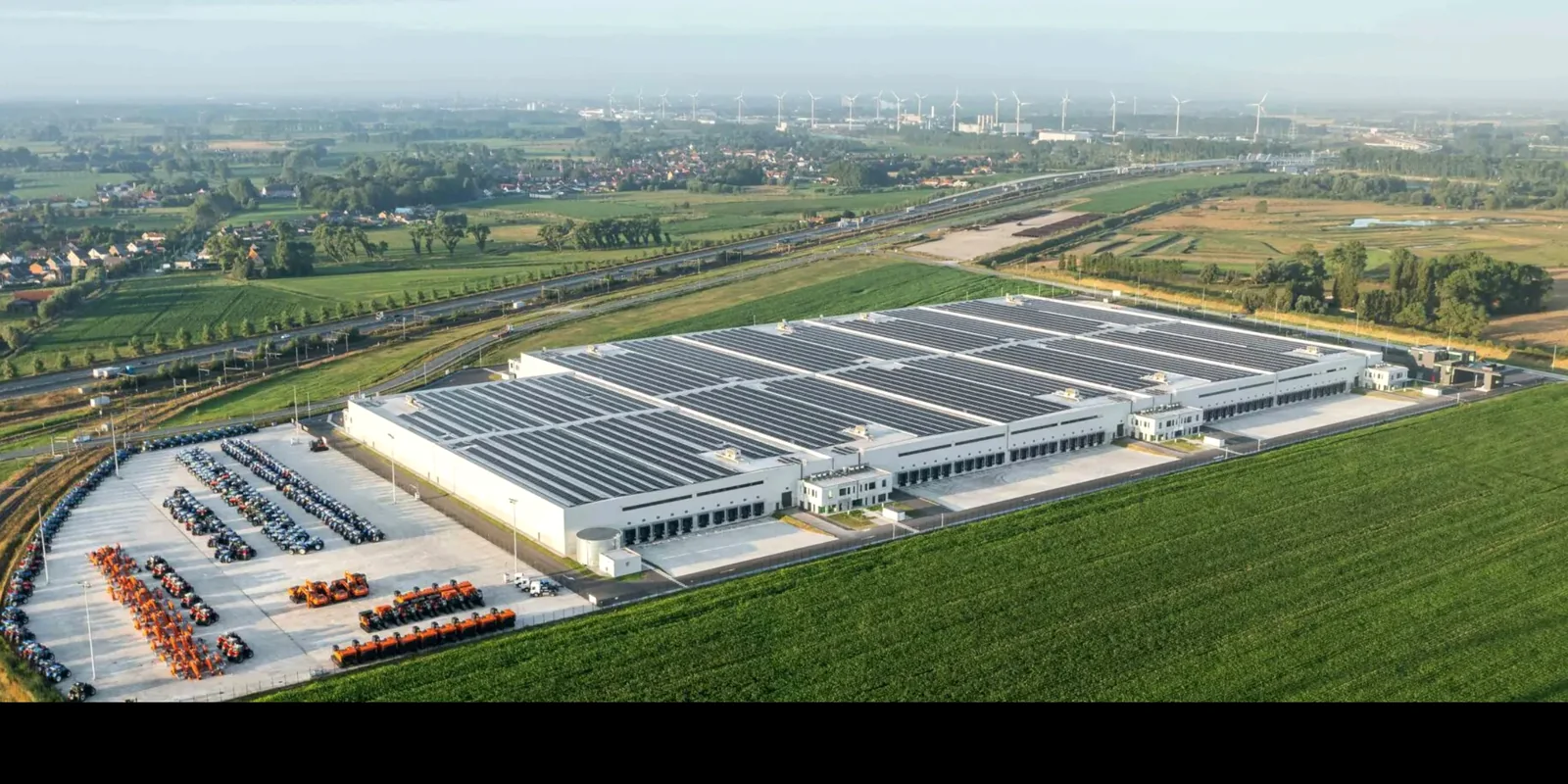 Luchtfoto van een industriële hal waarvan het volledige dak bedekt is met zonnepanelen, op een bedrijventerrein